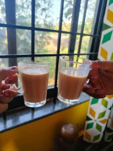 Zwei Personen halten Gläser mit Saft an einem Fenster. in der Unterkunft Service Apartment 1BHK in Ankola