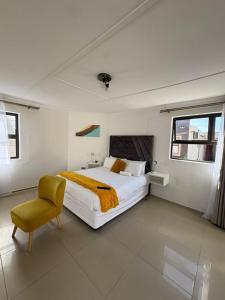 ein weißes Schlafzimmer mit einem Bett und einem Stuhl in der Unterkunft Suuka Guest House in Walvis Bay