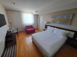 ein Schlafzimmer mit einem großen weißen Bett und einem rosa Stuhl in der Unterkunft Breaking Business Hotel in Mosciano SantʼAngelo