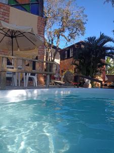 a large swimming pool with an umbrella and chairs at Pousada Gendra's in Imbituba