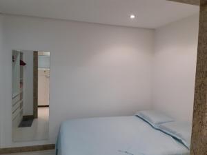 a white bedroom with a bed and a mirror at Kitnet acolhedora in Caxias do Sul