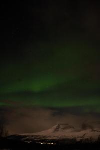 een noorderlicht in de lucht boven een besneeuwde berg bij Room in Cozy Cottage 