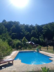 une piscine bleue avec un banc et des arbres dans l'établissement Cabañas Vega del Molino, à Linares