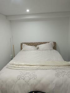 een wit bed met witte lakens en kussens bij Protea Place Cottage in La Mercy +2 foto's