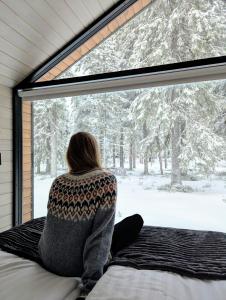 a woman sitting on a bed looking out of a window at Arctic Nest Forest Cabin in Kotila +53 photos