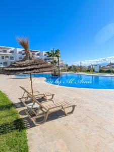 een paar ligstoelen met een parasol van stro en een zwembad bij EliteStay by Al Amir in Cabo Negro