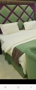 a bed with white and green sheets and pillows at تاج الملكه للشقق المخدومة in Ḑirs