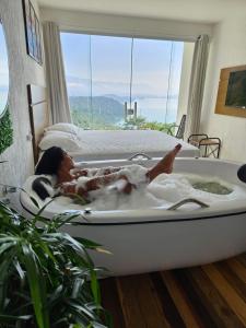 a woman laying in a bath tub in a room with a window at Alto da Piraquara Flat in Angra dos Reis