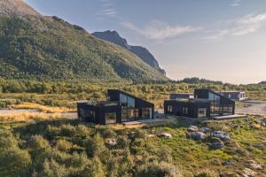 a house on a hill with mountains in the background at Hoda Cabin - Luxury lodge with jacuzzi and sauna in Lyngværet