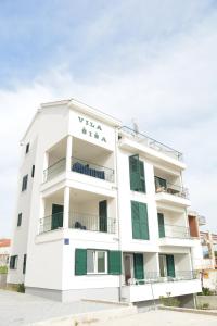 a white apartment building with green shutters at Beachfront Apartments Villa Šiša in Primošten