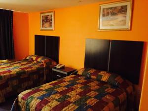 2 łóżka w pokoju hotelowym z pomarańczowymi ścianami w obiekcie Scottish Inn & Suites Hobby Airport w mieście Houston