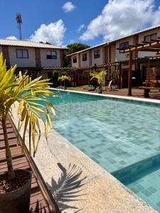 a swimming pool with a palm tree next to a building at 2 QUARTOS, Condomínio Villa de Rodes IMBASSAÍ Super bem localizado, Próximo a PRAIA, FARMÁCIAS, MERCADO E RESTAURANTES in Imbassai
