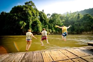 three people jumping off a dock into a river at River Kwai Jungle Rafts in Sai Yok