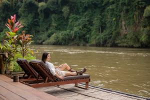 een vrouw op een bank naast een rivier bij River Kwai Jungle Rafts in Sai Yok