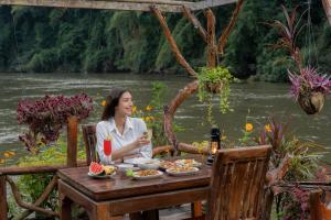 a woman sitting at a table with a drink at River Kwai Jungle Rafts in Sai Yok