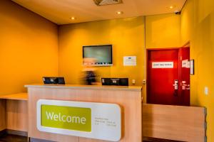 a welcome counter with a television on a yellow wall at ibis Budget Sydney Olympic Park in Sydney