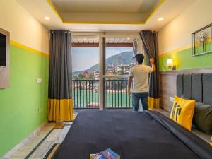 Ein Mann steht in einem Zimmer und schaut aus dem Fenster. in der Unterkunft The Hosteller Rishikesh, Laxman Jhula in Rishikesh
