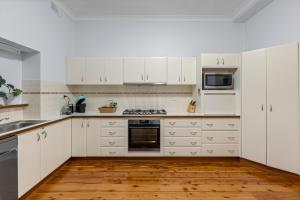 a white kitchen with white cabinets and a wooden floor at Cottage on Carthage in Tamworth