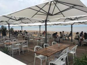 Mensen zitten aan tafels en stoelen onder parasols op het strand. bij Mezzanines 50 m de la plage in Châtelaillon-Plage