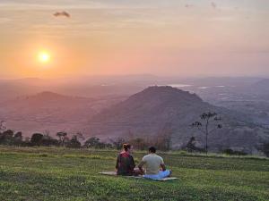 two people sitting on a field watching the sunset at Solar de Bonito - Casa Ingá in Bonito +1 photo