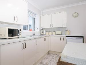 a white kitchen with white cabinets and a microwave at Green Bank in Dymchurch