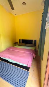 a bed in a yellow room with a pink blanket at D'pinggir Guest Room in Kuala Tahan