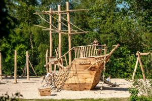 Ein Kind sitzt auf einem Holzspielplatz in der Unterkunft Stacaravan Camping It Wiid Earnewoude in Earnewâld