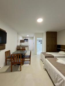 a bedroom with two beds and a table and a kitchen at Pousada Larimor in Boicucanga