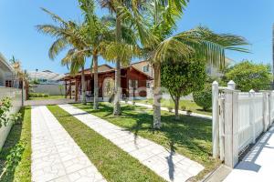 ein Haus mit Palmen vor einem Zaun in der Unterkunft Casa Aconchegante – A 200m da praia da Pinheira in Pinheira