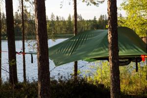 a green tarp hanging from trees near a lake at Capture Nordic Wilderness Camp - Baumzelt in Ilomantsi