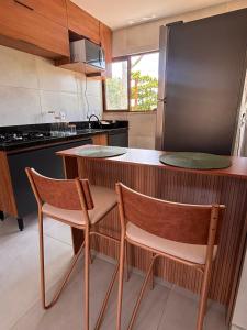 a kitchen with two chairs and a counter with a refrigerator at 2 QUARTOS, Condomínio Villa de Rodes IMBASSAÍ Super bem localizado, Próximo a PRAIA, FARMÁCIAS, MERCADO E RESTAURANTES in Imbassai