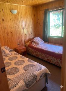 deux lits dans une chambre en bois avec une fenêtre dans l'établissement Cabañas los Jardines de Lican ray, à Licán Ray