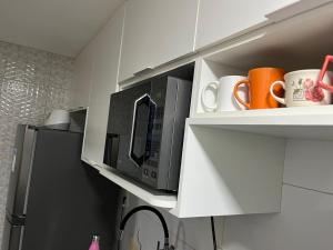 eine Mikrowelle in einem weißen Schrank mit Tassen und einem Kühlschrank in der Unterkunft Barra prime 1539 in Barra dos Coqueiros