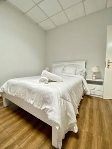 ein weißes Bett in einem Schlafzimmer mit Holzboden in der Unterkunft Maculusso City Stay in Luanda
