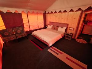 a bedroom with a large bed and a chair at Palki Camps and Resorts in Kailāna