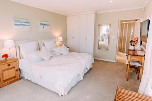 a bedroom with a large white bed and a desk at Dolphins' Playground Beachfront B&B in Plettenberg Bay