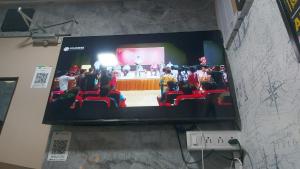 a flat screen tv with a group of people on a stage at Goldsport Dormitory in Jāmb