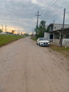 een witte auto geparkeerd aan de kant van een onverharde weg bij Kitnet das férias in Pontal do Paraná