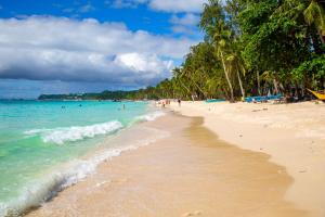 een strand met palmbomen en mensen in het water bij La Suerte Villa in Boracay