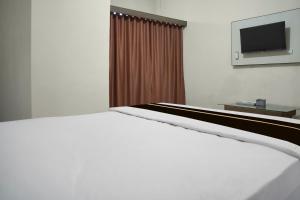a white bed in a room with a television at Hotel O Roda Inn in Padang