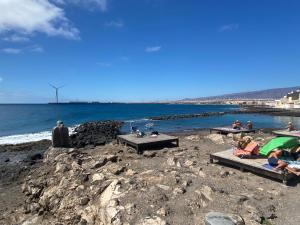 a group of people sitting on a beach near the water at MarMontaña in Arinaga