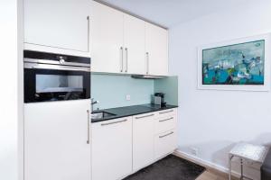 a white kitchen with white cabinets and a painting at Titlis Studio Engelberg with Balcony great View in Engelberg