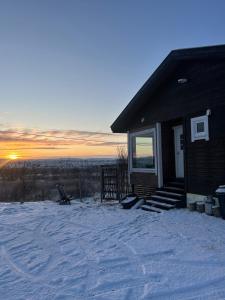 a house in the snow with the sunset in the background at Suovka reindeer & bird lodge in Varangerbotn