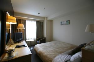 a hotel room with a bed and a desk with a television at Cypress Garden Hotel in Nagoya