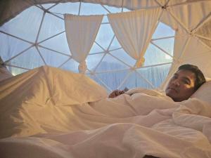 een man die in bed ligt in een iglo bij เวนิสบ้านเวร โดมใส in Ban Khun Nam Nan