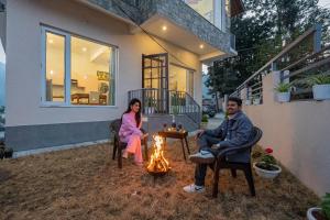 a man and woman sitting around a fire in front of a house at SaffronStays The Kumaoni Abode in Bhīm Tāl