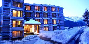 a building is covered in snow with mountains in the background at Lords Residency in Manāli