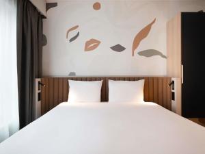 una camera da letto con un letto con lenzuola bianche e foglie sul muro di Adagio access Brussels Delta a Bruxelles Altre 69 foto