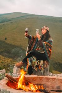 una donna seduta accanto al fuoco con in mano dei bicchieri di vino di Solarium Cabaña a Riobamba