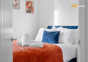 a white bed with an orange blanket and blue pillows at Comfortable 2 Bed Airdrie Flat w Private Parking in Airdrie